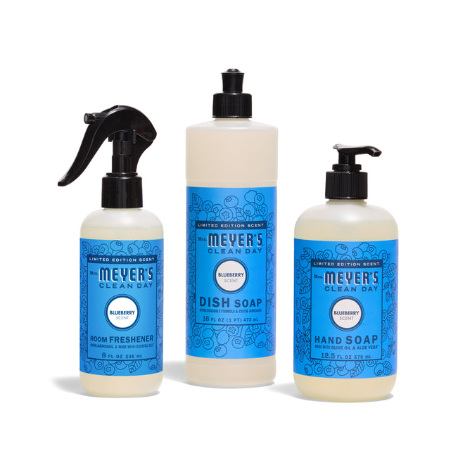 Three Mrs. Meyers Scents & Sun Essentials - Blueberry products—Hand Soap, Dish Soap with pump, and Room Refresher—stand upright in blue-labeled bottles on a white background, all featuring the limited edition blueberry scent.