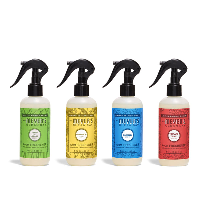 Four Mrs. Meyer’s Summer Room Freshener Collection bottles are shown in green (Fresh Cut Grass), yellow (Basil Lemon), blue (Bluebell), and red (Tomato Vine) with black sprayers.