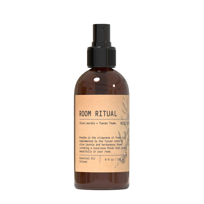 The Muse Apothecary Room Spray - Olive Collection features Tuscan thyme and olive laurel notes in a brown glass bottle with a black nozzle and minimalist beige label adorned with botanical illustrations.