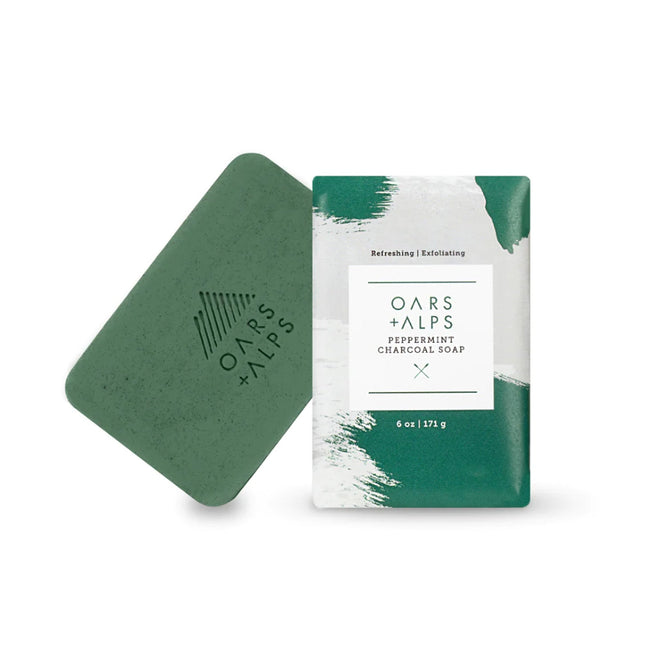 A 6 oz. green Oars + Alps Charcoal Bar Soap, shown beside its white and green Peppermint Charcoal Soap packaging. Infused with peppermint oil and activated charcoal for a refreshing, invigorating cleanse.