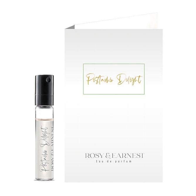 A small clear spray vial labeled “Pistachio Delight” by Rosy & Earnest stands beside a matching card, both displaying this vegan eau de parfum sample’s indulgent pistachio scent.