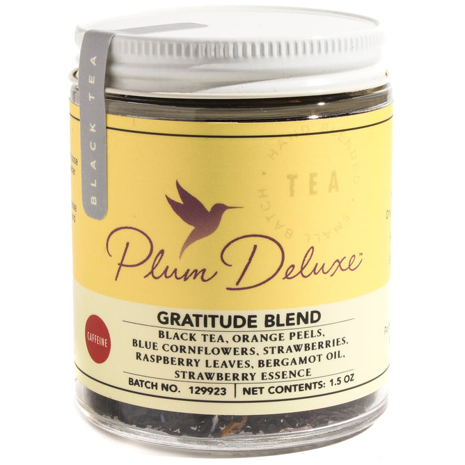 A jar of Plum Deluxe Gratitude Strawberry Earl Grey Tea with a yellow label, featuring black tea blended with orange peels, blue cornflowers, strawberries, raspberry leaves, and bergamot oil.