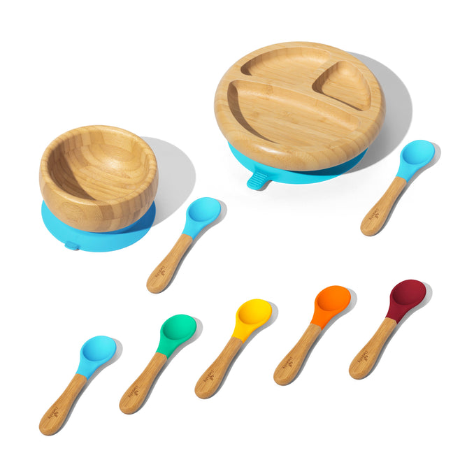 The Grove Collaborative Essentials Baby and Toddler Dish Set includes a bamboo bowl and divided plate with blue suction bases plus seven bamboo-handled baby spoons featuring silicone heads in blue, teal, green, yellow, orange, red-orange, and red.