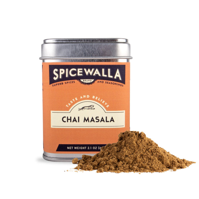 A Spicewalla Chai Masala tin sits beside a small mound of loose chai masala powder, showcasing this aromatic Indian spice blend against a white background.