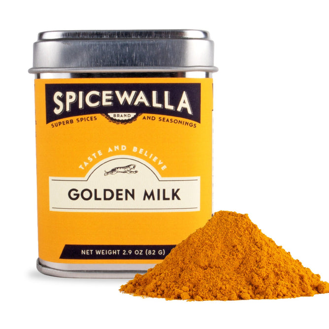 A Spicewalla Golden Milk tin with a silver lid and an orange-yellow label stands behind a mound of bright yellow powder, suggesting a flavorful turmeric-based drink rich in antioxidants.