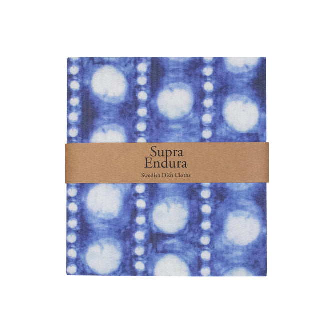 The Swedish Dishcloth Tie Dye by Supra Endura is a sustainable kitchen cleaning cloth made from cellulose and cotton, featuring a blue and white tie-dye pattern, wrapped in a brown paper band labeled Supra Endura.