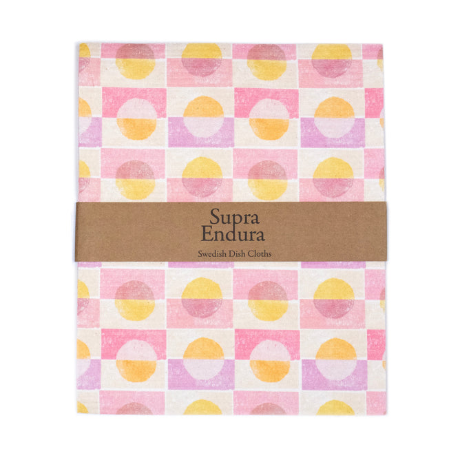 The Large Block Print Swedish Dishcloth by Supra Endura is made from sustainable cellulose and cotton, featuring a geometric design with pink, yellow, and white squares and circles. It is wrapped in a brown paper band labeled Supra Endura Swedish Dish Cloths..
