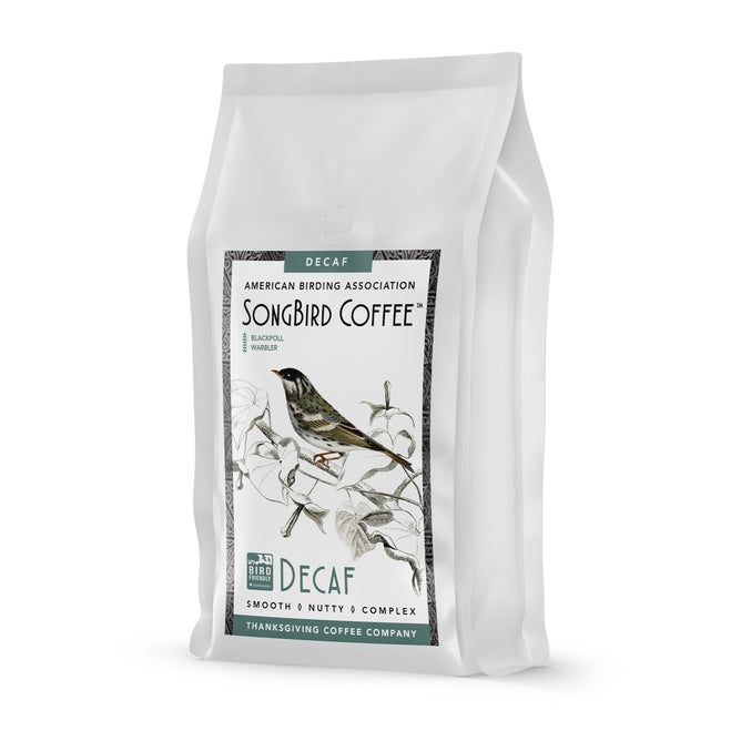 The Songbird Decaf Medium by Thanksgiving Coffee features a white package with a bird on branches. This Bird Friendly® coffee from Mexico is smooth, nutty, and complex. Associated with the American Birding Association, it promotes sustainable coffee practices.