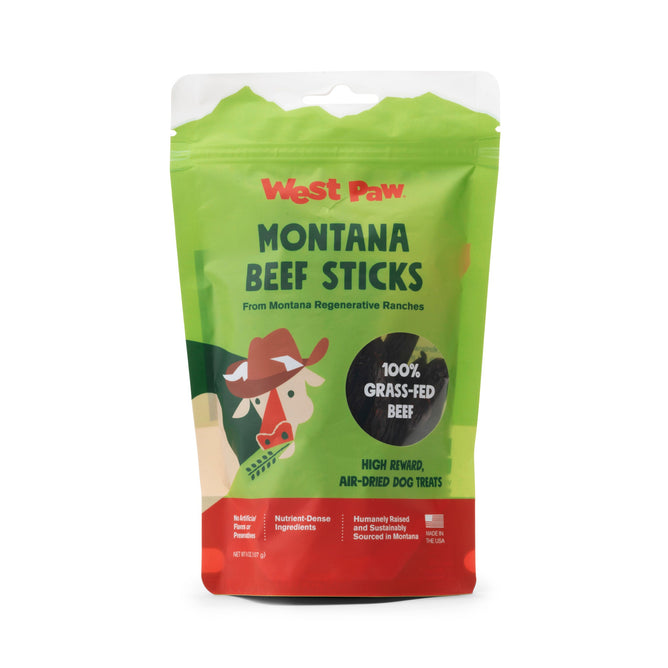 A green and red resealable bag of West Paw Montana Beef Sticks made from 100% grass-fed beef, air-dried for dogs, features a cartoon cow and rancher. Packaging highlights beef sourced from regenerative ranches for a natural treat.