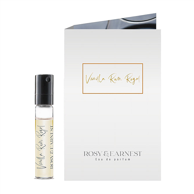 A small Vanilla Rum Royal sample spray vial stands beside a white card with the name in gold script and Rosy & Earnest Eau de Parfum below, evoking the fragrances rich vanilla notes.