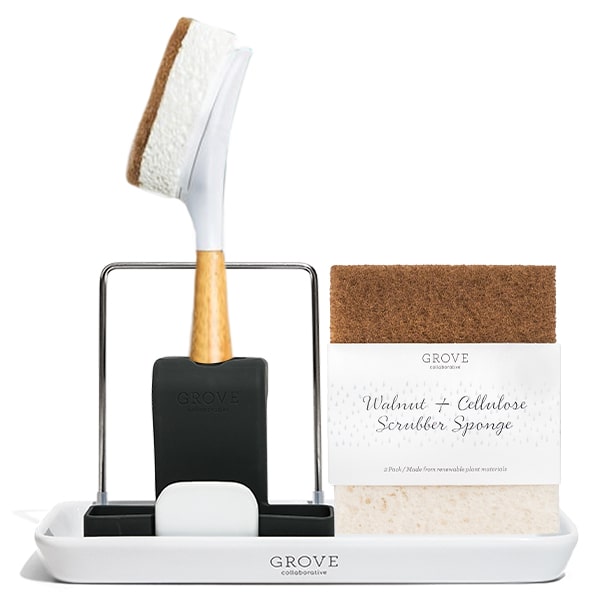 The sinkside-tool-set by Grove Collaborative includes a white ceramic holder branded with Grove, a wooden-handled dish brush, and two walnut and cellulose scrubber sponges.