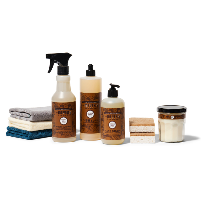 The autumn-abode-starter-set-mmcd by Grove Collaborative includes Mrs. Meyers multi-surface spray, dish soap, hand soap, sponges, folded cloths, and a candle. These items are neatly arranged against a white background.