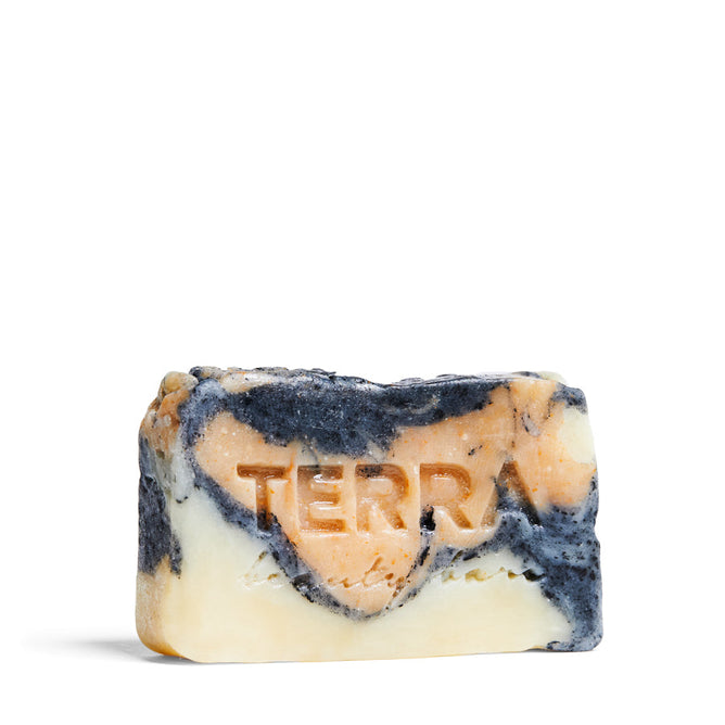 A close-up reveals a rectangular soap bar with a marbled black, orange, and cream design. The Marble Activated Charcoal Facial Bar with Brazilian Yellow Clay by Terra Beauty Bars rests on a plain white background, highlighting its elegance.
