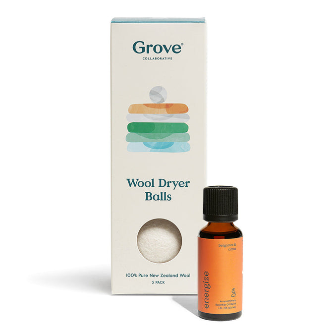 A package of Grove Co. Wool Dryer Balls sits next to a small Energize essential oil bottle, both with colorful graphics emphasizing their chemical-free promise. The oil bottle showcases vibrant orange and black hues, while the packaging highlights Bergamot & Citrus.