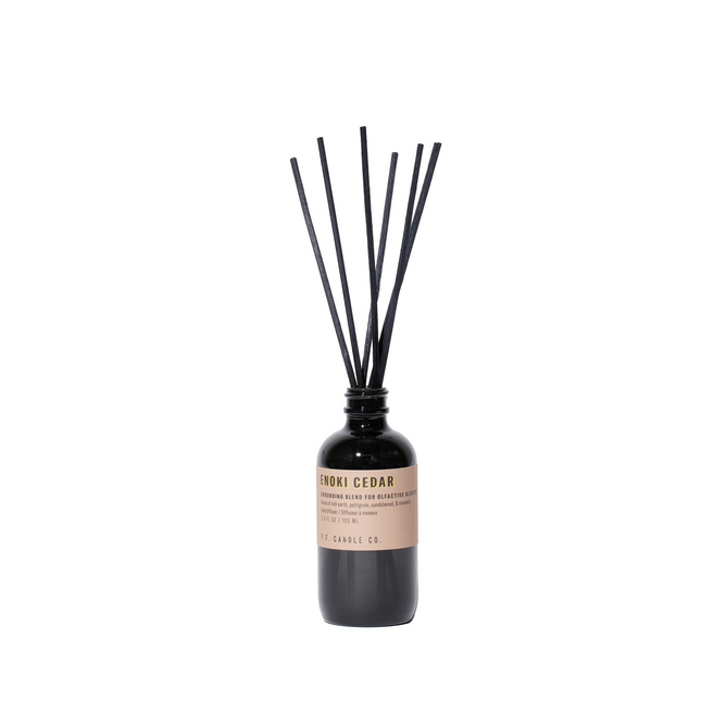 P.F. Candle Co.s Alchemy Reed Diffuser labeled Hinoki Cedar showcases black reed sticks in a sleek black bottle set against a white background, offering a nature-inspired fragrance that brings tranquility and elegance to any space.