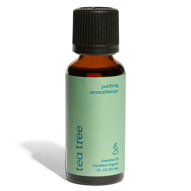 A small brown bottle with a green label from Grove Co. reads Organic Tea Tree Essential Oil - Purifying Aromatherapy. It highlights 1 fl oz (30 ml) of certified organic tea tree oil, and features a ribbed black cap for grip.
