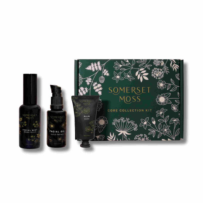 The Somerset Moss Core Collection Kit features a green box with floral designs, containing three essentials upfront: rejuvenating facial mist, luxurious facial oil, and nourishing balm tube, housed in dark bottles with elegant gold text.