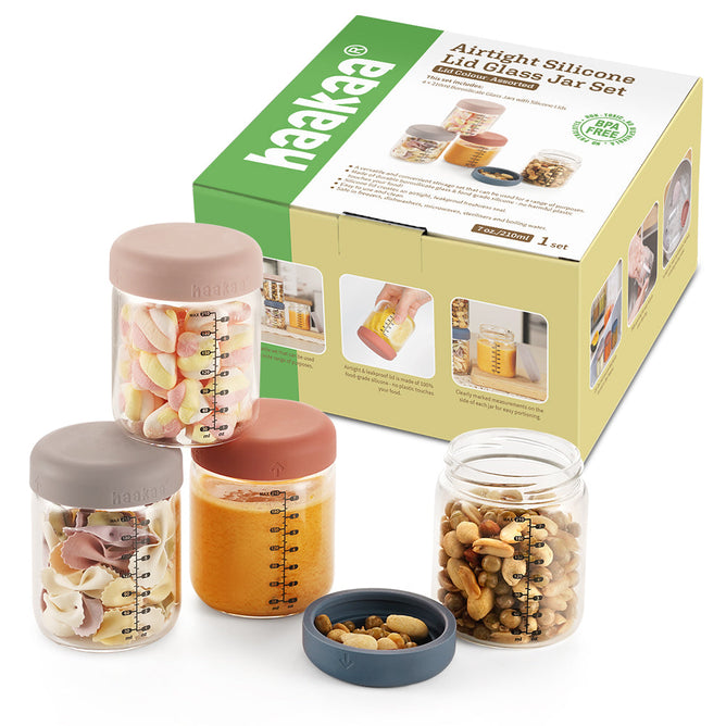 Three Haakaa glass jars with silicone lids, ideal for reusable glass container needs, hold marshmallows, sauce, and mixed nuts. Situated before packaging labeled Glass Baby Food Storage Jar Set, the jars include measurement markings and usage tips for homemade meals.