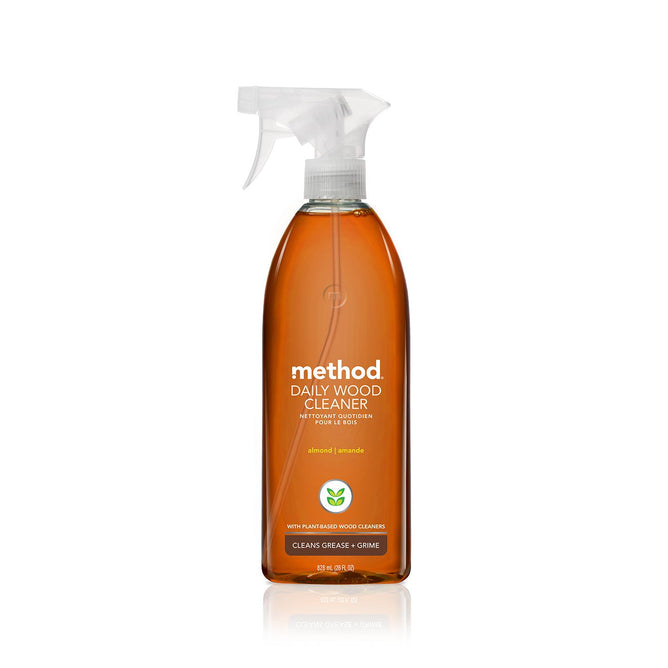 A clear spray bottle of methods Daily Wood Cleaner in almond scent features cruelty-free, plant-based ingredients. The amber liquid contrasts with minimalist white text and logo. Made from recycled plastic, this eco-conscious cleaner effectively tackles grease and grime.