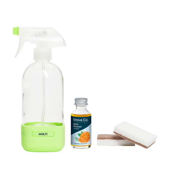 The Grove Co. Countertop Cleaning Set features a clear spray bottle with a green base labeled MULTI, a Glass Cleaner Concentrate bottle with an orange illustration, and two scrub pads including a Walnut Scrubber Sponge, all arranged against a white background.