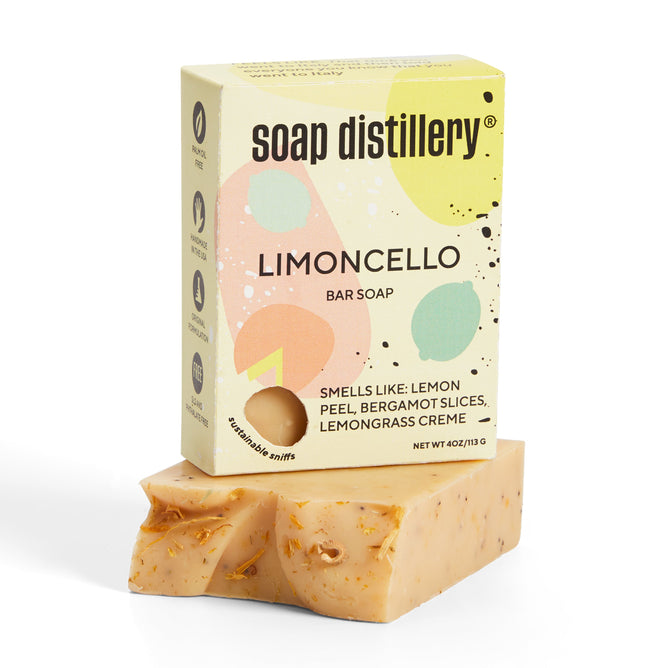 Soap Distillerys Limoncello bar soap, a palm oil-free product, features colorful abstract packaging and an aromatic scent of lemon peel, bergamot slices, and lemongrass creme. The bar has a natural look with visible flecks.