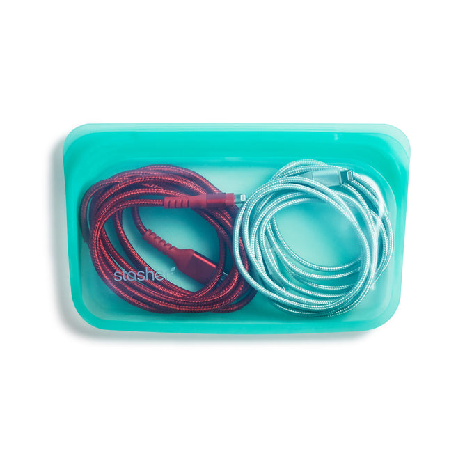 A turquoise Reusable Silicone Snack Bag by Stasher, made from premium food-grade silicone, elegantly cradles two neatly coiled, non-toxic charging cables—one vibrant red and the other calming light blue—on a plain white background.