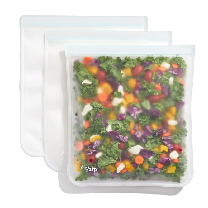 The Flat Gallon Bag Kit by (re)zip includes three reusable silicone bags with double-lock closures for freshness. The front bag displays a colorful mix of chopped veggies like carrots, kale, and cabbage.