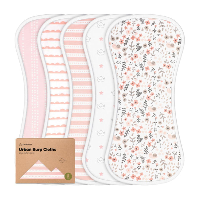Five colorful, gender-neutral burp cloths by KeaBabies—featuring flowers, stripes, clouds, and stars—are shown with a KeaBabies Organic Cotton Burp Cloths - 5 pack brown cardboard package. These GOTS-certified sustainable cloths are perfect for eco-conscious parents.