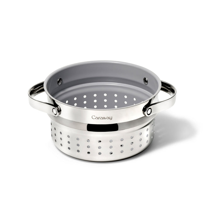 The Caraway Stainless Steel Sauce Pan Steamer, 3 qt, features a sturdy base, two handles, and a branded logo. With evenly spaced holes for effective draining, it complements Caraways non-toxic collection for practical and stylish healthy cooking.