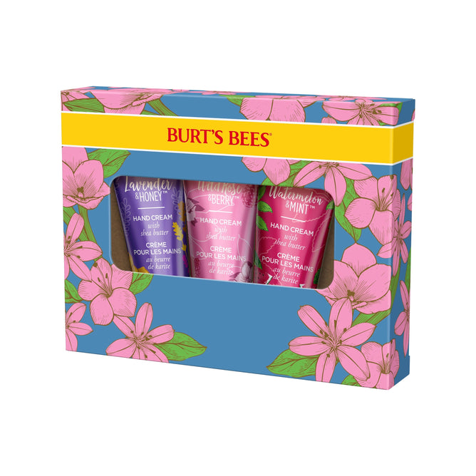 The Burts Bees Hand Cream Trio Gift includes three luxurious hand creams in Lavender & Honey, Wild Rose & Berry, and Watermelon & Mint scents. Packaged in a floral box with pink flowers on a blue background and a yellow band, all are crafted with a Natural Origin Formula.