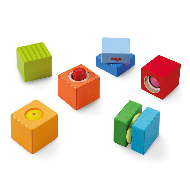The Fun with Sounds - Wooden Discovery Blocks by HABA are eco-friendly, colorful blocks that enhance sensory development. They feature unique elements like grooves, buttons, and discs in vibrant red, blue, green, orange, and yellow on a white background.