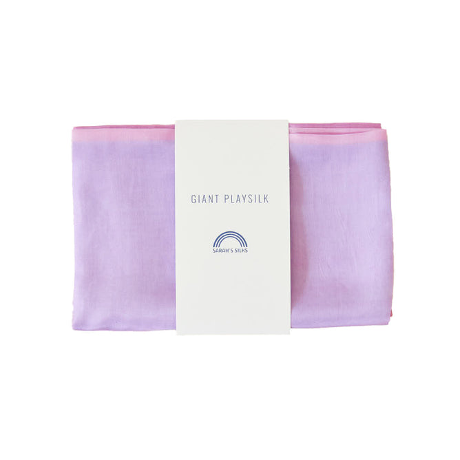 A folded lavender to pink Giant Playsilk from Sarahs Silks, perfect for open-ended play in Montessori & Waldorf homes, features a white label with a rainbow logo reading GIANT PLAY SILK.