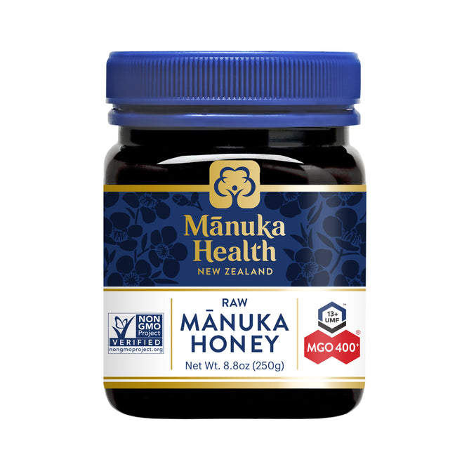 A jar of Manuka Health Manuka Honey MGO 400+ / UMF 13+, featuring a blue lid and floral-patterned label, is Non-GMO Project Verified with MGO 400+ potency and weighs 8.8 oz (250g).