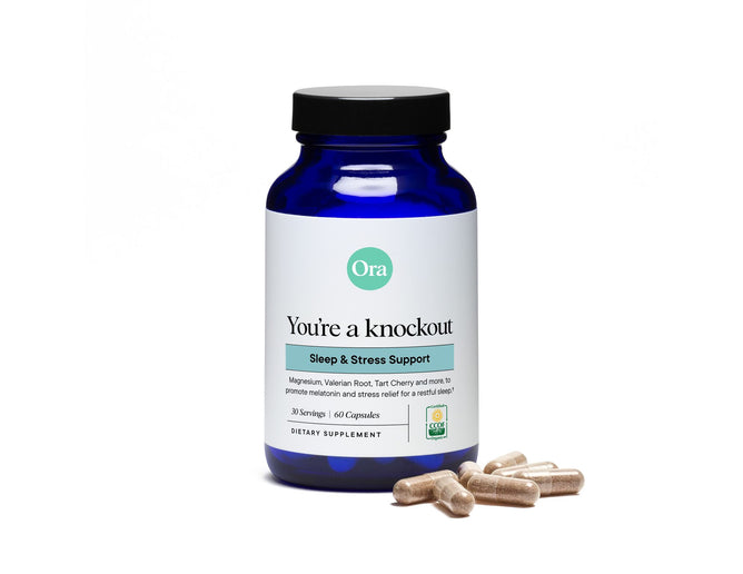 A blue bottle labeled Youre a knockout with a white label featuring green and black text contains Ora Organics Sleep Aid Supplement, made from plant-based ingredients like magnesium, valerian root, and tart cherry. Several capsules rest beside the bottle.