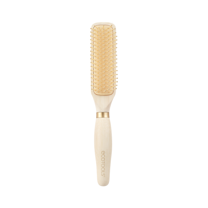 The EcoTools Eco Curl Activating Brush is a rectangular paddle hairbrush with a light wooden handle, beige bristles, and a gold accent at the base. The handle is printed with ecotools, highlighting its identity as a sustainable brush designed for gentle care.