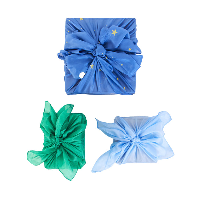 Three gifts are elegantly wrapped using Sarahs Silks Reusable Gift Wrap Furoshiki Set, showcasing sustainable wrapping. The top gift in starry blue fabric rests above green and light blue ones, each tied with large knots for an eco-friendly touch.