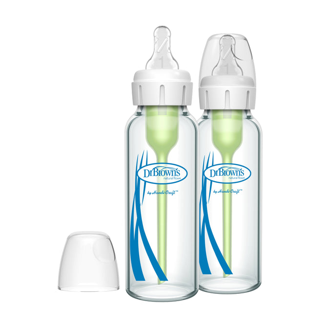Two Dr. Browns Glass Baby Bottle Natural Flow® Anti-Colic Options+™ with green internal vent systems and breast-like Level 1 Slow Flow Nipples display blue logos; clear plastic caps accompany them, with one cap lying beside the bottles.