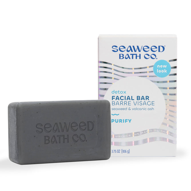 A rectangular gray soap bar embossed with The Seaweed Bath Co sits before its packaging, showcasing the Detox Purifying Facial Bar. With seaweed, charcoal powder, and volcanic ash, it promises purer skin against a light background featuring the brands name.