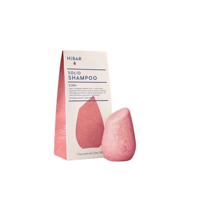 The HiBAR Curl Shampoo is a pink teardrop-shaped solid bar next to its white and pink package, which highlights rice protein and fermented tomato extract for enhanced hair care.