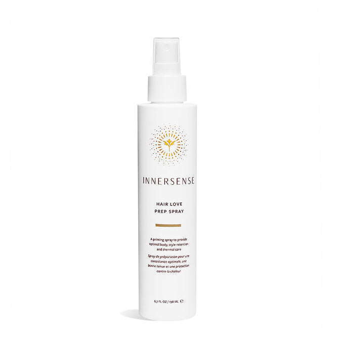The Hair Love Prep Spray by Innersense Organic Beauty is in a white bottle with a spray nozzle, featuring a minimalist design. The packaging includes product information and a yellow sunburst logo above the brand name, enriched with organic aloe vera for nourishing care.