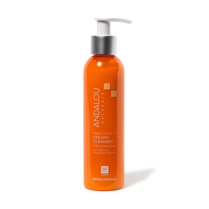 An orange bottle of Andalou Naturals Brightening Meyer Lemon + C Creamy Cleanser with a silver pump showcases its vitamin C skin brightening benefits on the label, along with the Clean Brand Project Purity Award logo at the bottom.