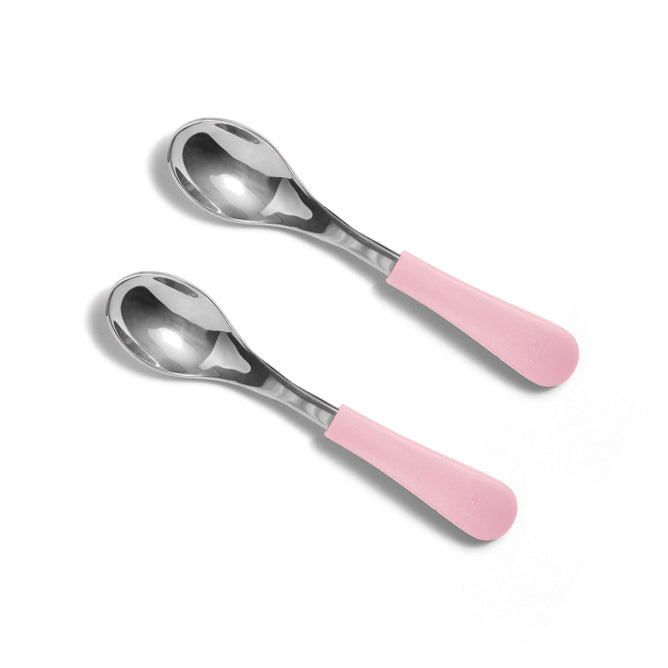 Two Avanchy Stainless Steel Baby Spoons for 4+ months, featuring smooth, reflective surfaces and light pink ergonomic handles, are placed diagonally on a plain white background. Eco-friendly and non-toxic, these spoons provide style and safety for your little one.