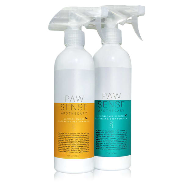 Two eco-friendly bottles of Paw Sense Waterless Pet Shampoo & Stain and Odor Remover: the front features an oatmeal mango scent with an orange label, and the rear offers a lemongrass coconut scent with a teal label. Both have clear spray tops for easy, waterless cleaning.