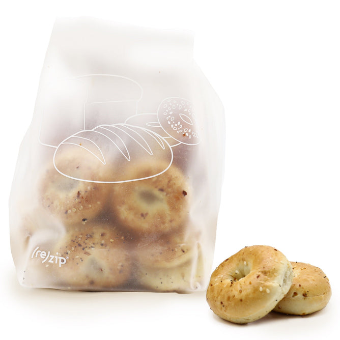The (re)zip Reusable Bread & Pantry Roll Top Bag, crafted from food-grade PEVA and featuring bread and doughnut designs, stands upright with two bagels on a white surface in front. Its TerraCycle-friendly for an eco-conscious choice.