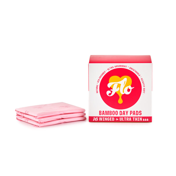 Beside three individually wrapped pink pads, a package of FLO Bamboo Day Pads by Here We Flo highlights its natural, biodegradable, and ultra-thin features and includes 16 hypoallergenic winged pads.