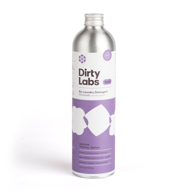 The silver bottle, featuring a purple and white label, showcases Dirty Labs Bio Laundry Detergent with Phytolase®, offering an eco-friendly formula scented with Jasmine, Matcha, and Vetiver for your laundry.