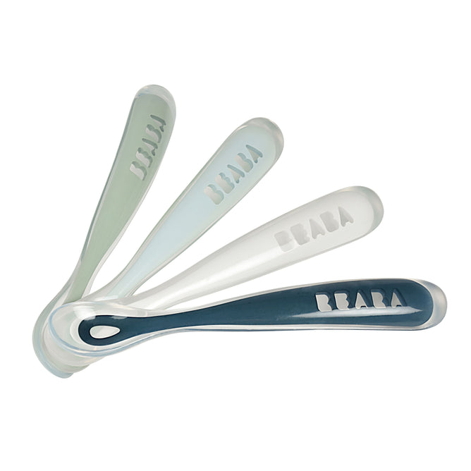 A set of four BEABA First Foods Silicone Spoons, in green and blue tones, are arranged fan-like. The translucent handles feature the BEABA brand name, ideal for introducing solids.