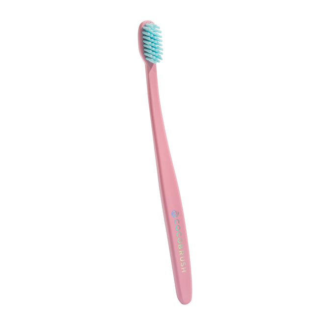 A pink Cocobrush Toothbrush by Cocofloss, featuring soft light blue multi-density bristles and a handle marked COCOBRUSH in white, stands upright against a plain white background, promising support for healthy gums.