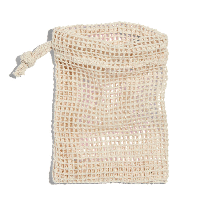 A beige Soap Saver Bag by Peach, crafted from GOTS-certified cotton, lies flat on a white background. It features an open top with a drawstring on the left. Its slightly translucent mesh texture is perfect for lathering soap and exfoliating.