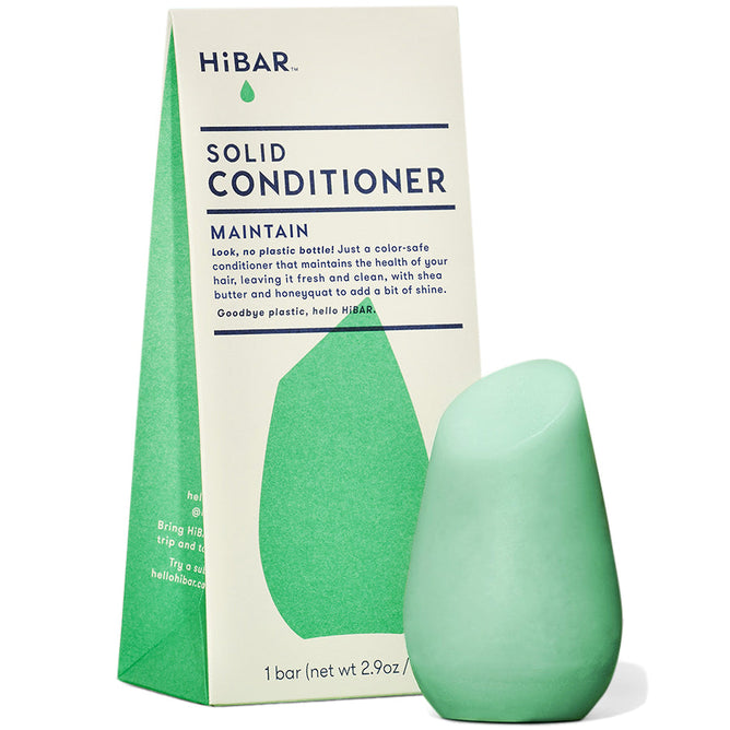 A green, teardrop-shaped HiBAR Maintain Solid Conditioner bar sits in front of its box, which is light green and blue. The packaging emphasizes eco-friendliness and highlights the benefits for dry hair with its natural ingredients.